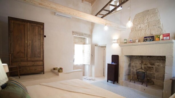 A spacious bedroom with a large bed, a wooden wardrobe, a stone fireplace, and a loft area with a wooden beam ceiling. - Dimora Storica   Nonna Adelina (Corigliano D'otranto)