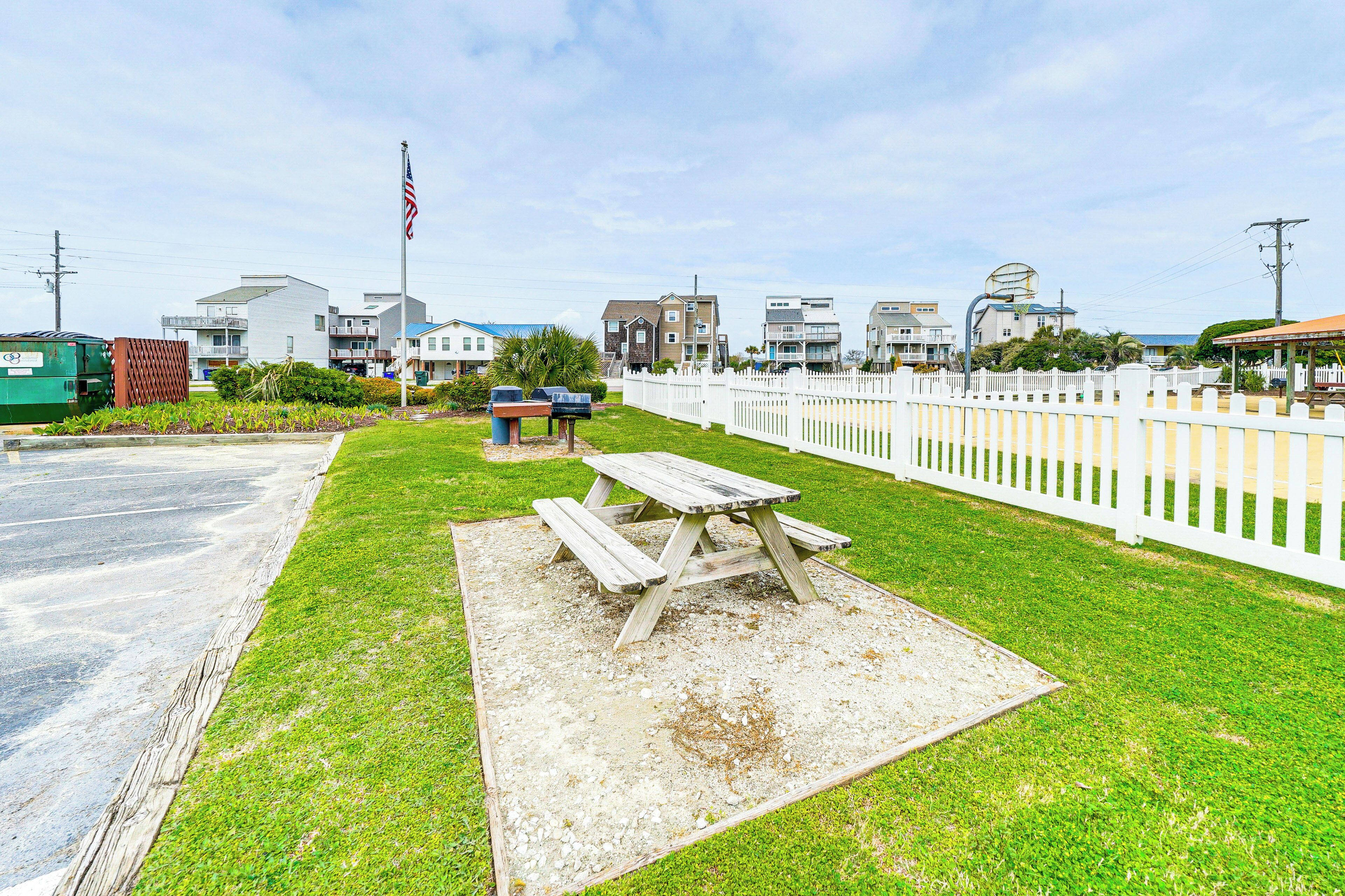 A picnic table in a grassy area with a white picket fence and houses in the background.