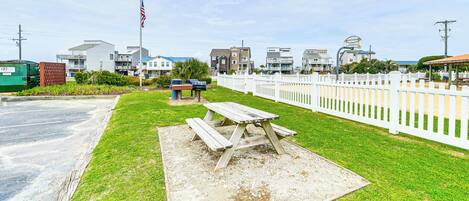 A picnic table in a grassy area with a white picket fence and houses in the background.