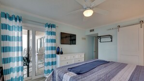 Un dormitorio con cama, ventilador de techo, puerta corredera de cristal y cómoda blanca.