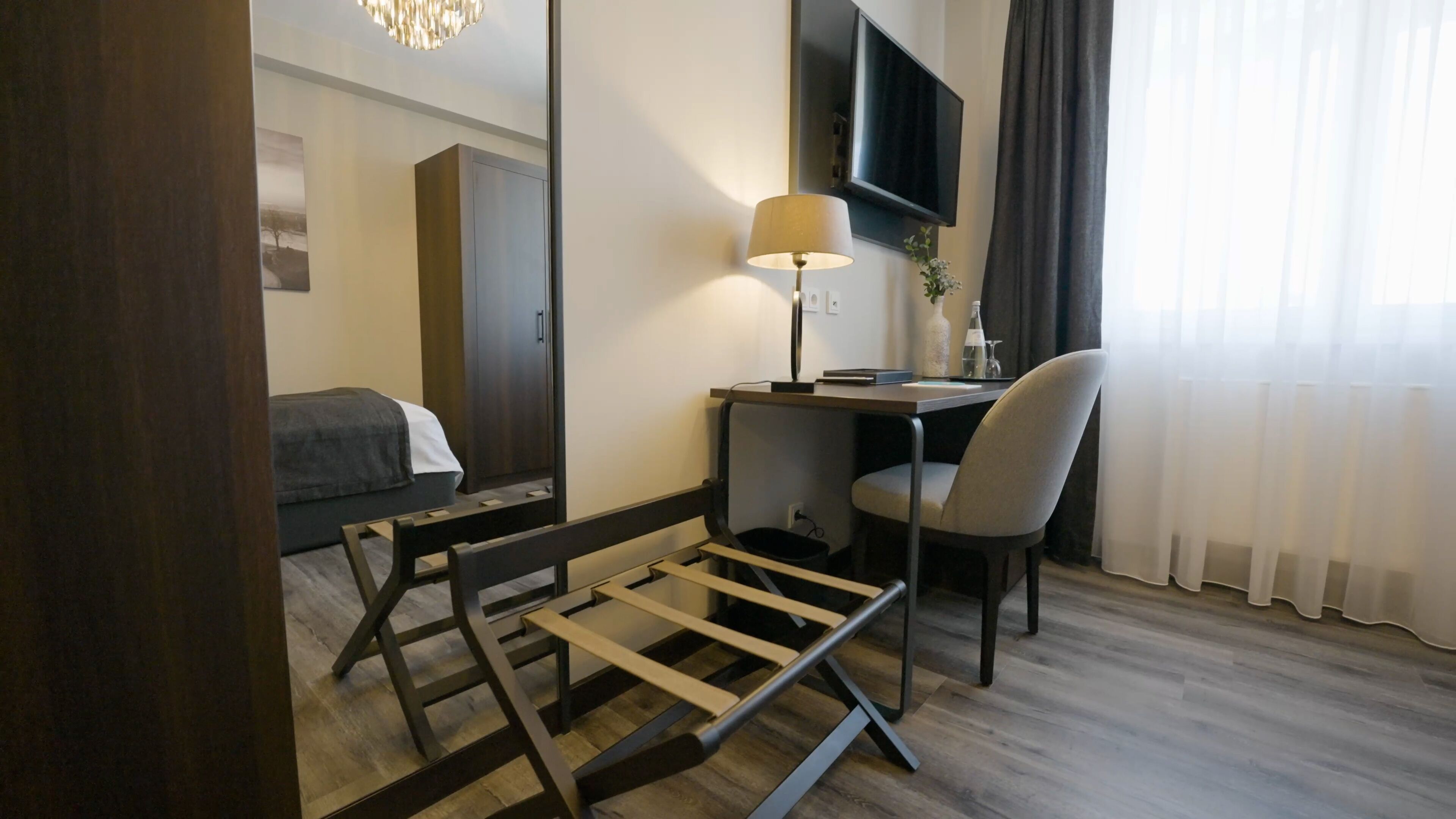 A hotel room with a bed, desk, chair, TV, and a mirror.