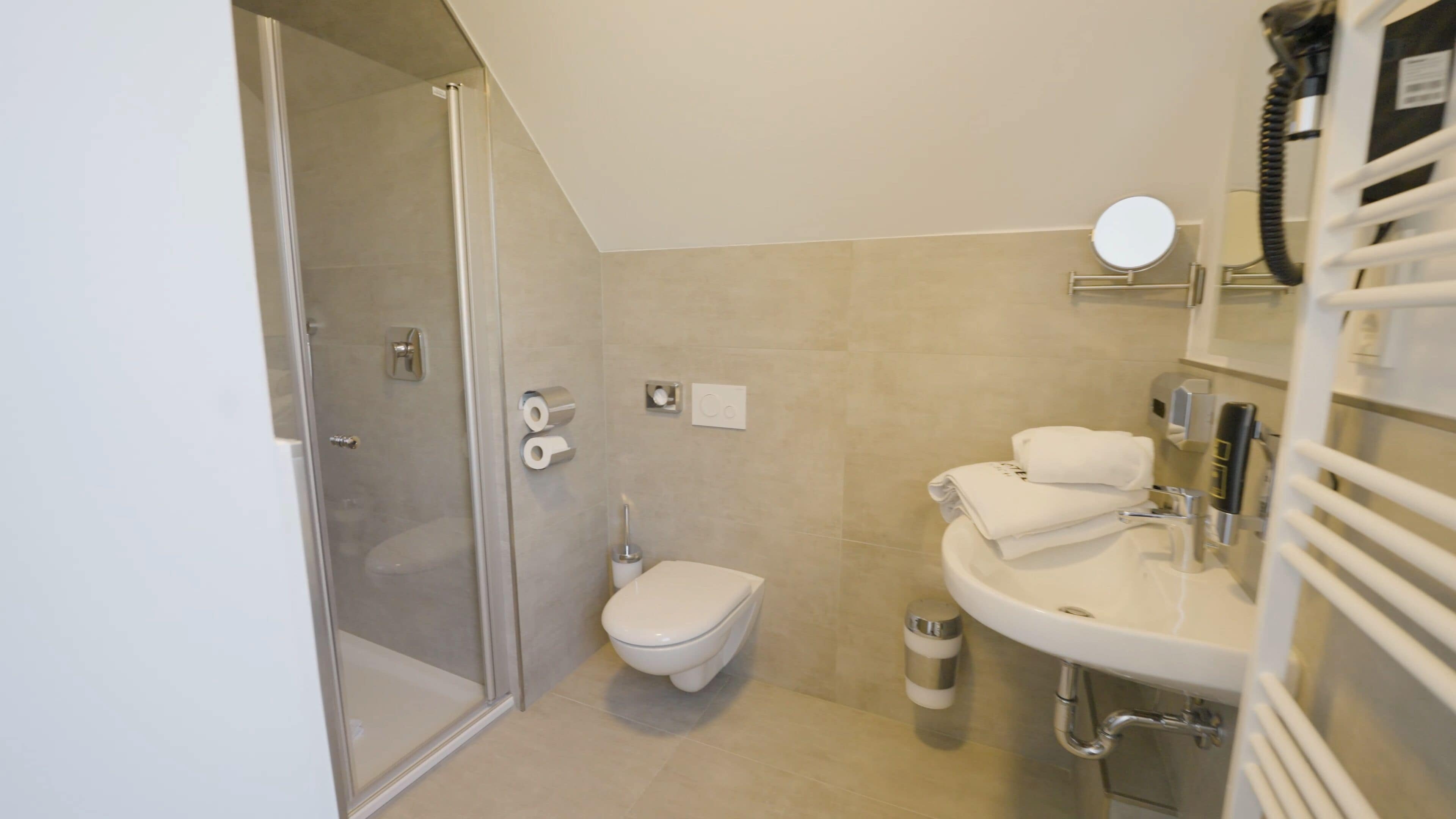 Un bany modern amb una cabina de dutxa de vidre, un vàter i un rentapeus amb barra de tovalloles.
