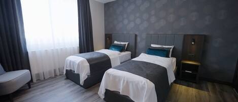 A hotel room with two beds, a chair, a bedside table, and a large window with curtains.