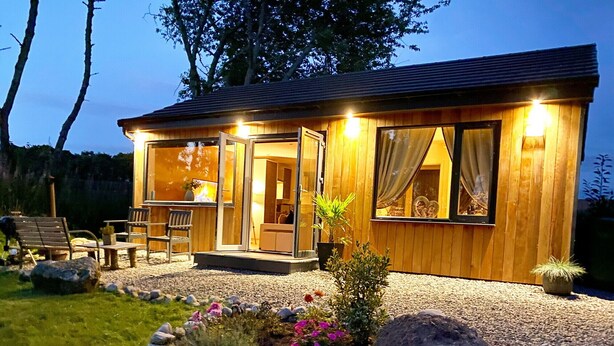 A wooden cabin with a glass door entrance, a small porch, and outdoor seating.