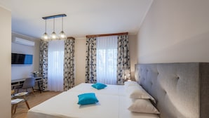 Camera d'albergo con un letto grande, due cuscini, una scrivania con una sedia, una TV e una finestra con tende a motivi.