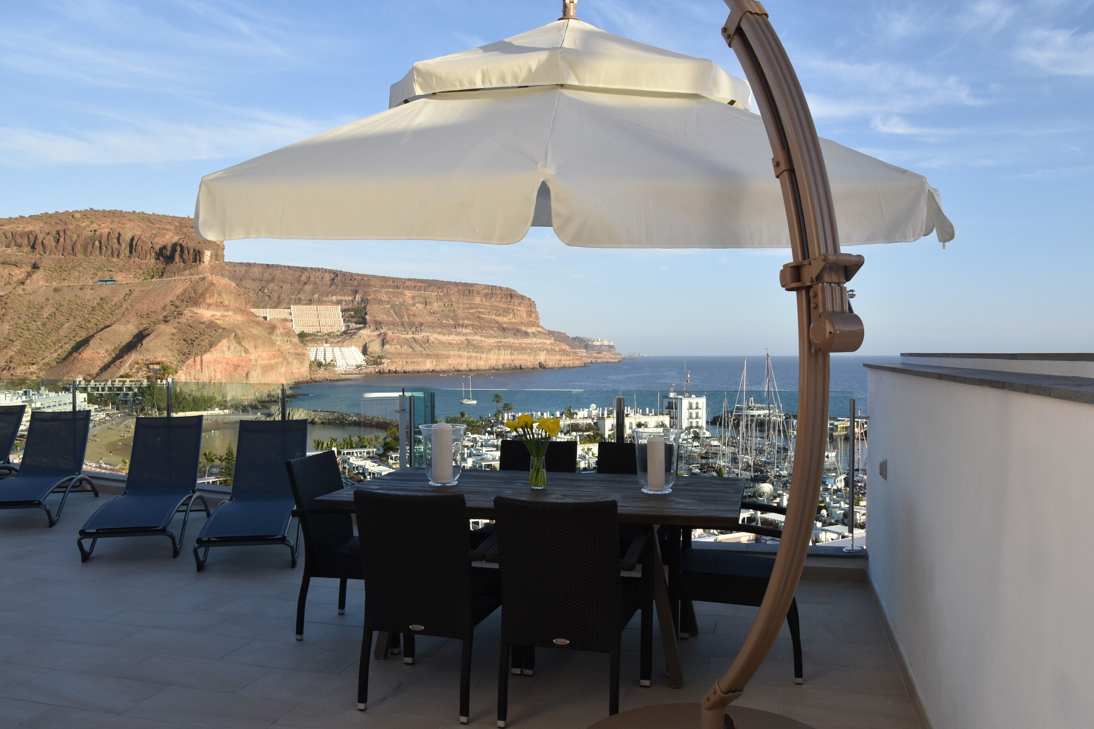 Terraço com mesa e cadeiras, vista para um porto e falésias.