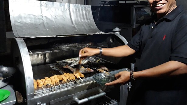 Una persona asando comida en una parrilla industrial en una cocina.