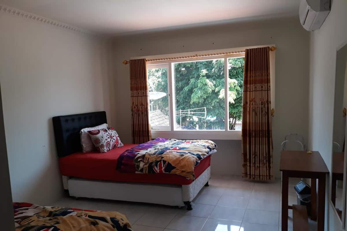 A bedroom with a bed, a window with curtains, a small table, and a chair.