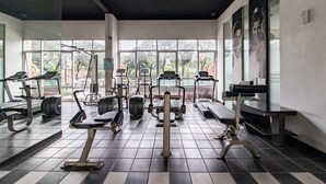 Un gimnasio con diverso equipo de ejercicio, ventanas amplias y piso de baldosas.