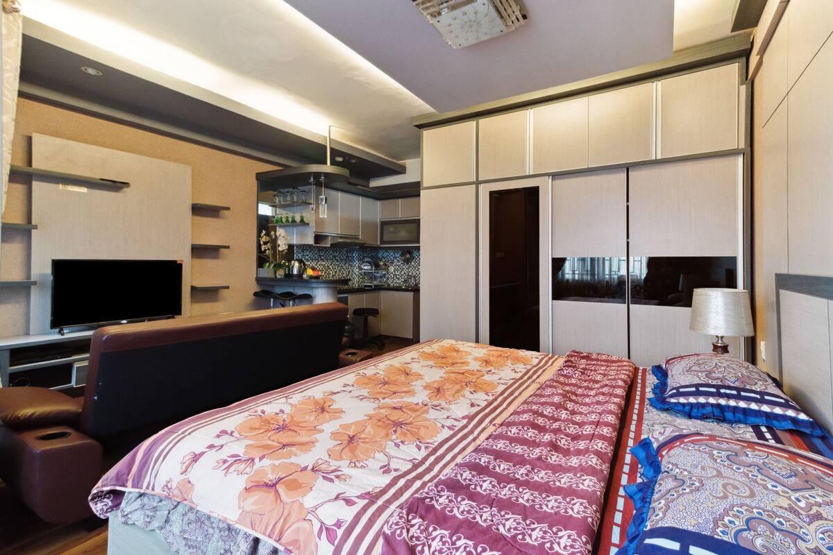 Una habitación de hotel moderna con una cama grande, un escritorio, un televisor y una kitchenette.