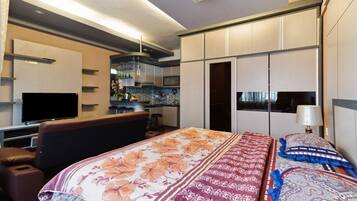 Una habitación de hotel moderna con una cama grande, televisión, kitchenette y baño.