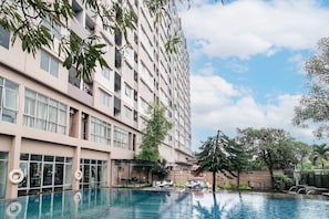 Un hotel de varios pisos con piscina, zona de estar al aire libre y vistas a la vegetación circundante.