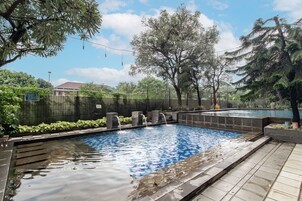 Una piscina con borde de piedra, rodeada de árboles y una valla.