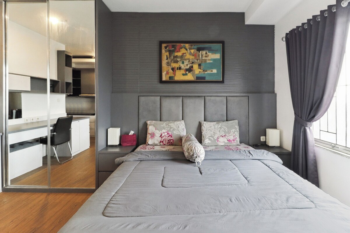 A modern bedroom with a bed, a desk, and a painting on the wall.