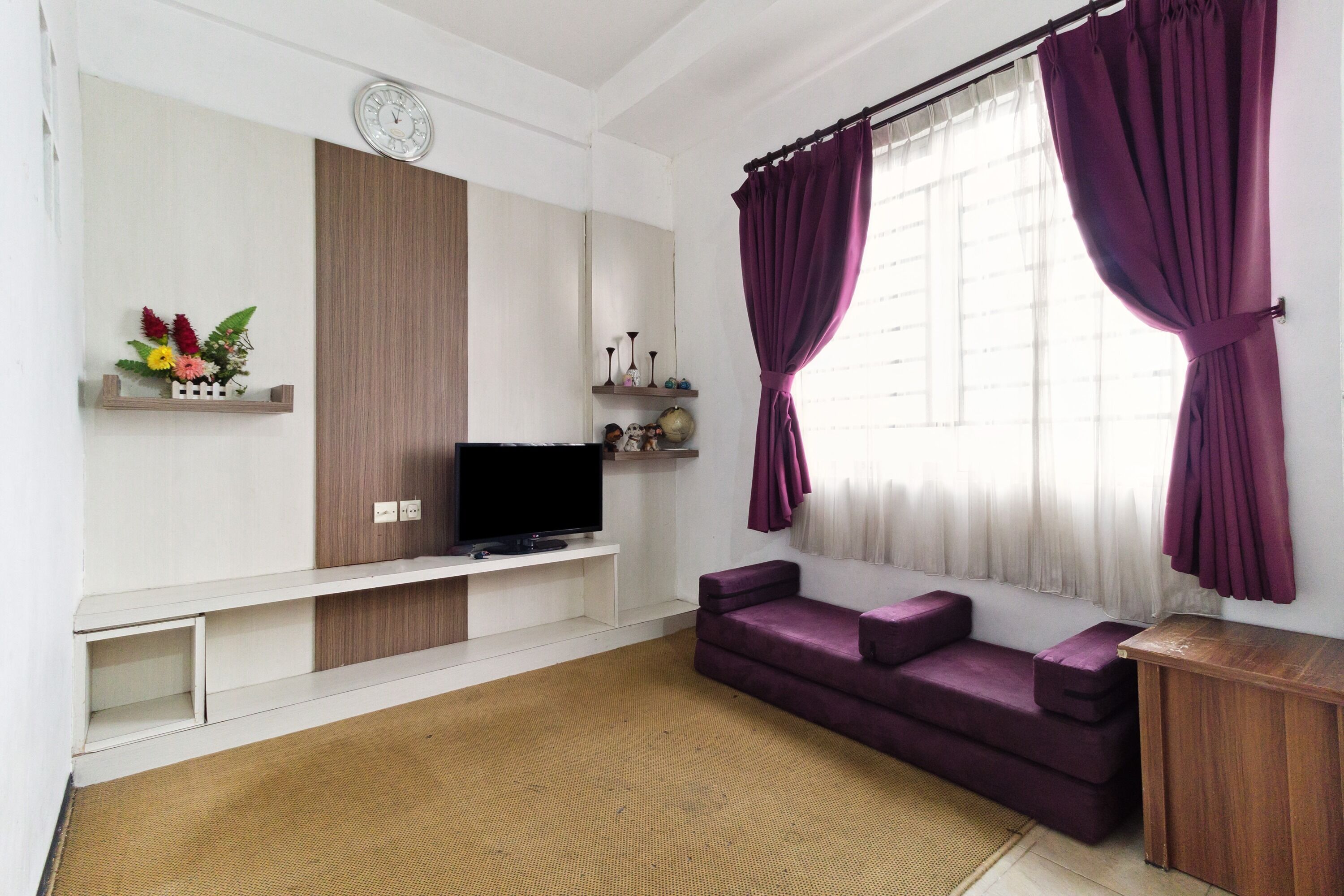 A living room with a flat-screen TV, a sofa, a coffee table, a decorative plant, and a window with curtains.
