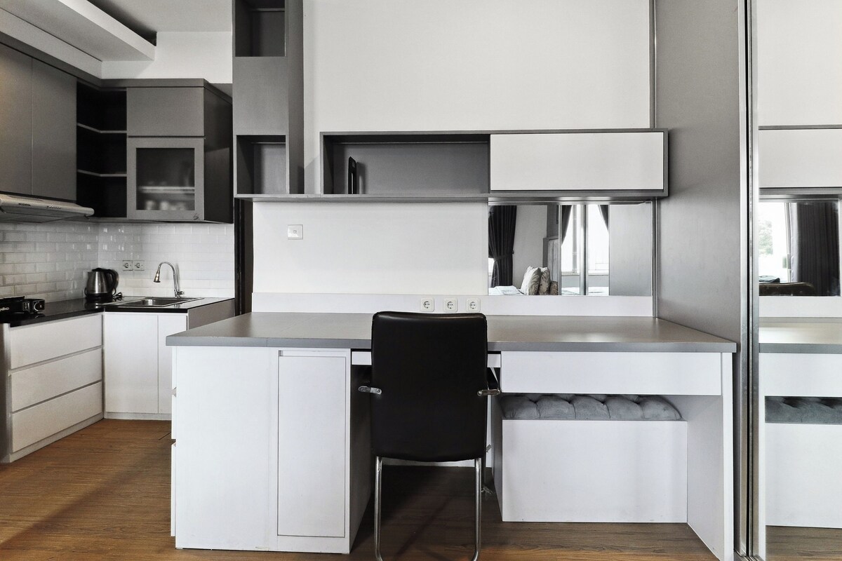 A modern kitchen with white cabinetry, a black chair, and a built-in island with a sink.