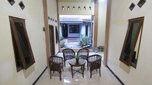 Un pasillo con zona de comedor, que incluye una mesa redonda y cuatro sillas, conduce a un patio exterior con techo de baldosas y plantas en macetas.
