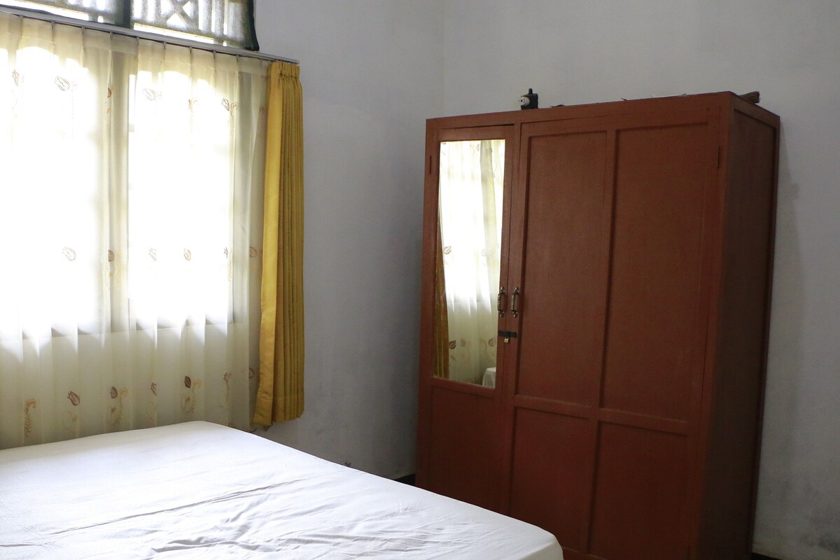 Una habitación con cama, armario y ventana con cortinas.