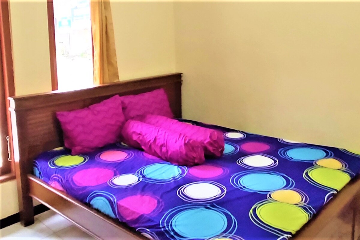 Ein Bett mit einer bunten Bettdecke im Kreismuster und zwei rosa Kissen.
