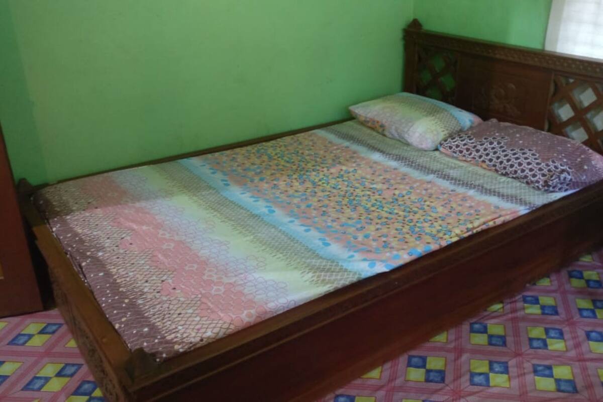 A single bed with a patterned bedspread and pillows, a wooden headboard, and a colorful floor pattern.