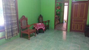 A room with green walls, a wooden chair, a small table with a red cloth, and a door with a yellow frame. - Adji Homestay - Hostel (Muntuk)