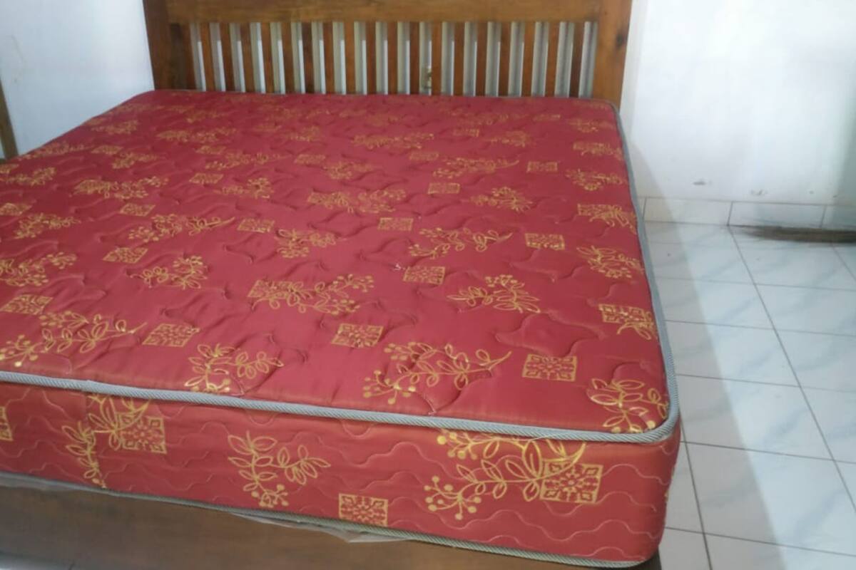 A bed with a red mattress featuring gold patterns, a wooden headboard, and a tiled floor.