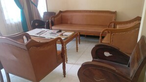 A living room with a sofa, two wooden chairs, and a coffee table with papers and pens. - Pringsewu Craft Homestay - Hostel (Muntuk)
