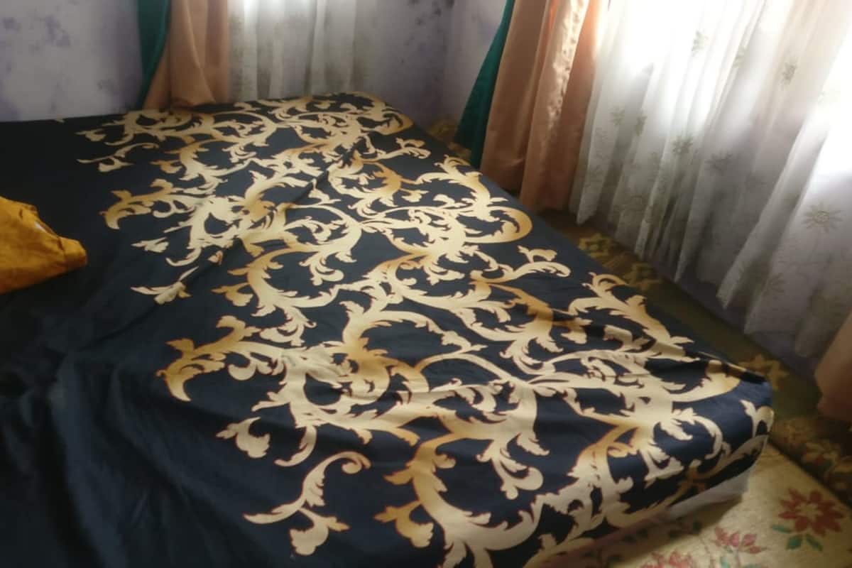 A bed with a dark blue and gold patterned bedspread, a yellow pillow, and curtains with a floral pattern.