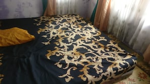 A bed with a dark blue and gold patterned bedspread, a yellow pillow, and curtains with a floral pattern. - Pringsewu Craft Homestay - Hostel (Muntuk)
