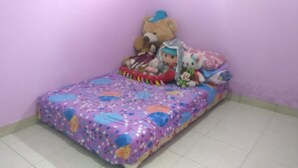 A small, neatly made bed with a colorful bedspread and a teddy bear on it. - Yati Homestay - Hostel (Muntuk)