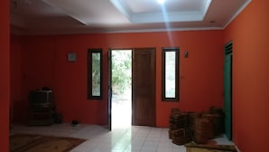 A room with red walls, a wooden door, and a tiled floor. There is a television and a pair of shoes on the floor. - Wahyu Homestay - Hostel (Muntuk)