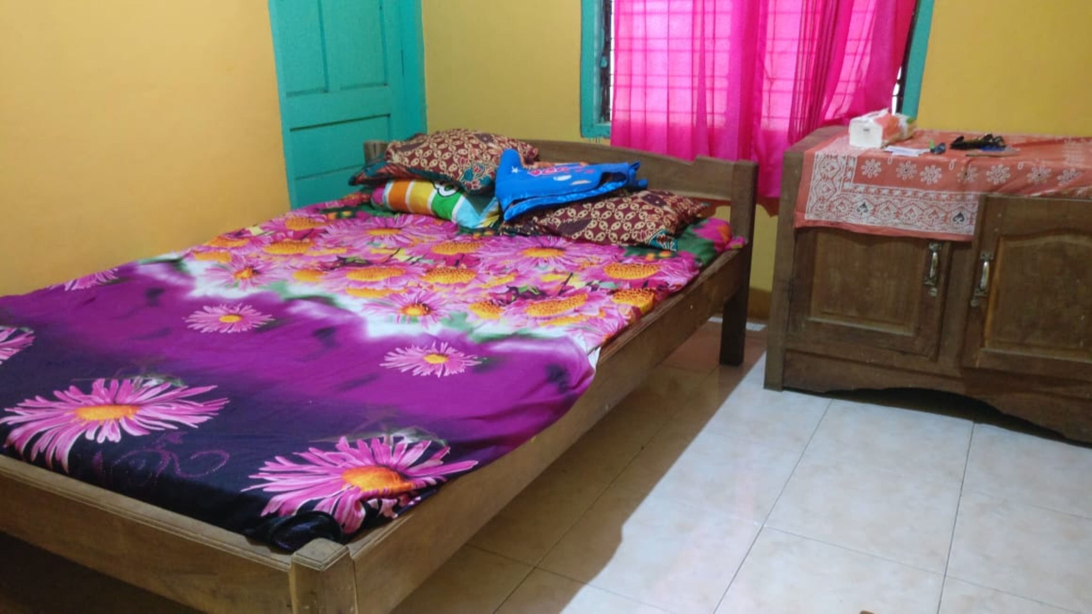 Un lit avec une couvre-lit à motifs floraux, une tête de lit en bois et une table de chevet en bois recouverte d’une nappe à motifs.