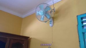 A room with a ceiling fan, a wooden cabinet, and a blue-framed window. - Wahyu Homestay - Hostel (Muntuk)