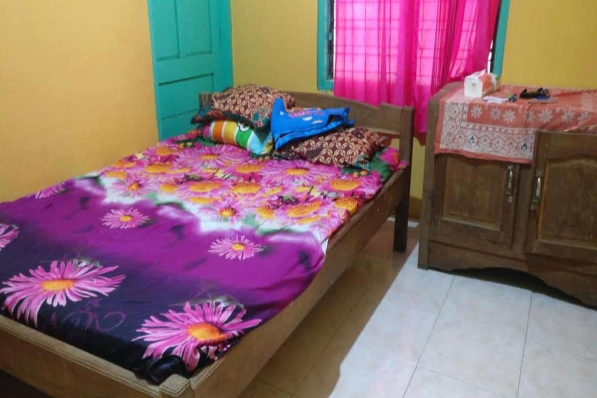 A bedroom with a bed covered in a floral bedspread, a wooden wardrobe, and a window with pink curtains.
