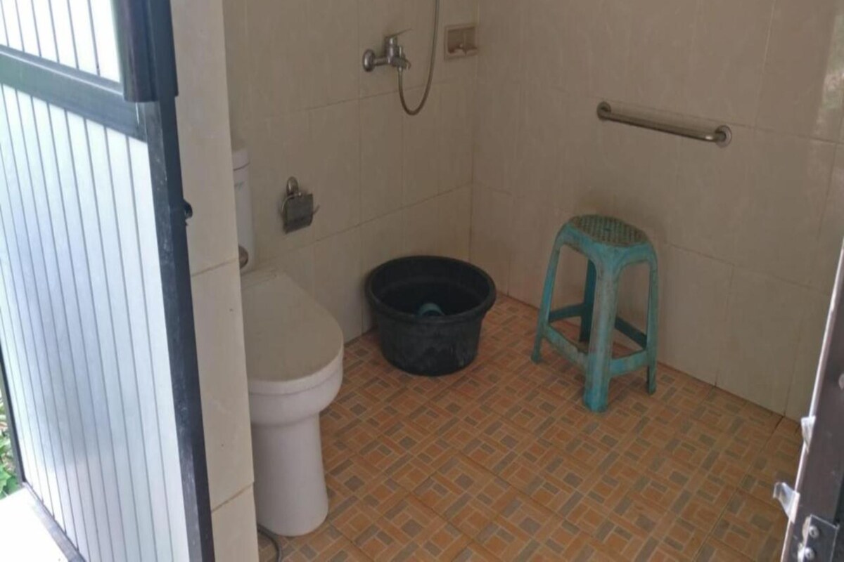 A small bathroom with a toilet, a black bucket, and a blue stool.