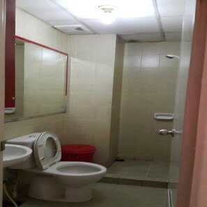 A small bathroom with a toilet, a red trash bin, and a mirror.