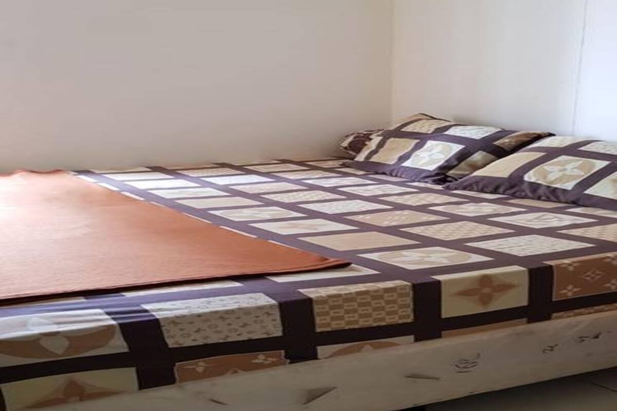 Una cama con colcha estampada y almohadas, una manta marrón y un cabecero blanco.