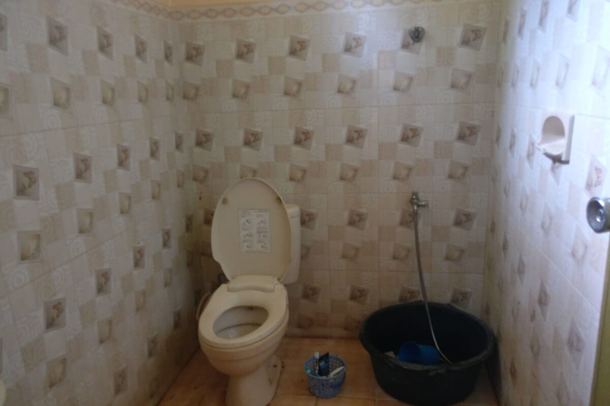 A small bathroom with a toilet, a bucket, and a cleaning brush.