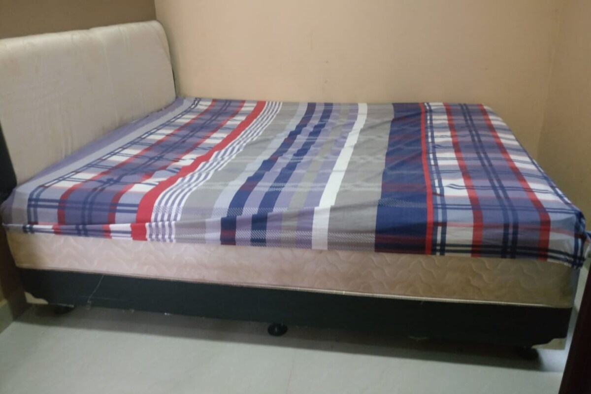 A small, single-bed room with a plain mattress and a simple, striped blanket.