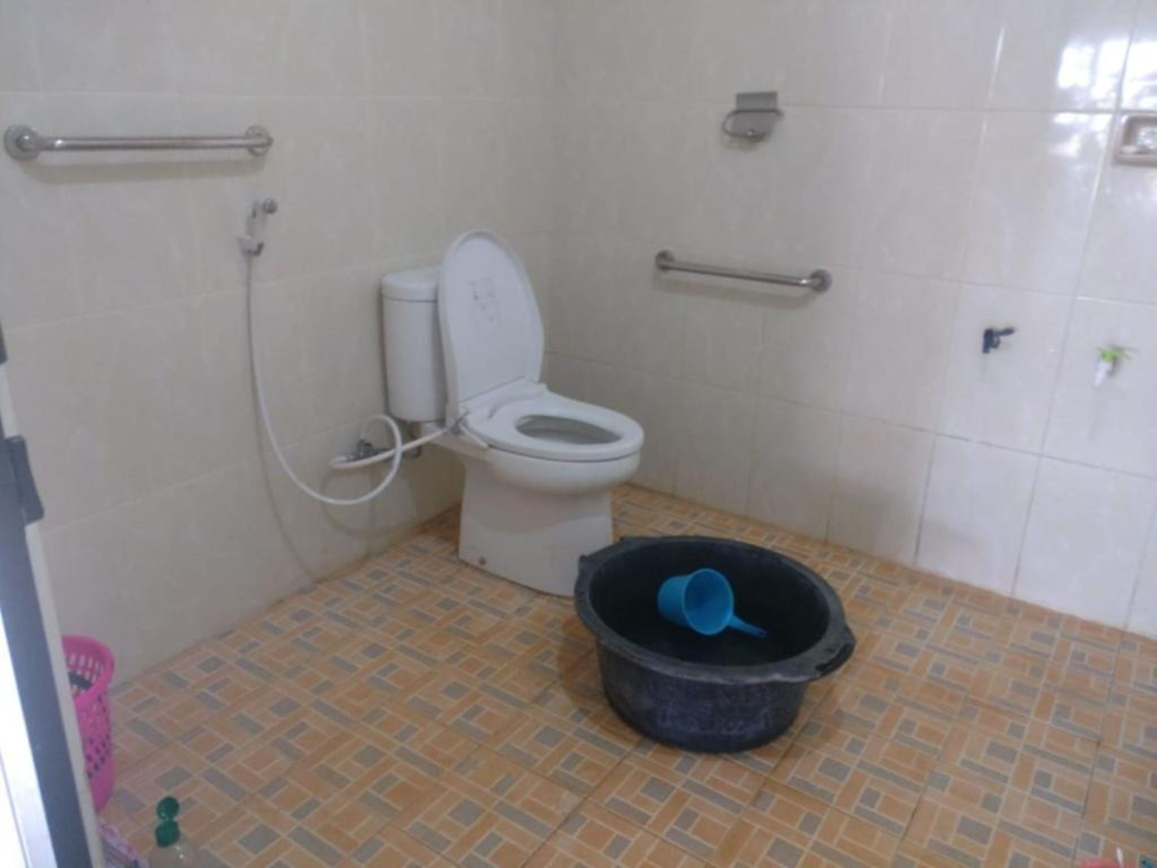 Une petite salle de bain équipée de toilettes, de barres d’appui, d’une douche et d’une poubelle.