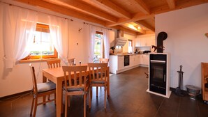 A cozy kitchen with wooden beams, a dining area with chairs, and a fireplace.