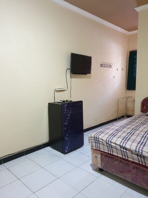 A bedroom with a bed, a TV mounted on the wall, a small cabinet, and a metal rack. - Griya Sekar Wangi (Surabaya)