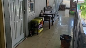 Un espacio exterior cubierto con piso de baldosas, una mesa con sillas, un contenedor de basura y un pequeño armario.