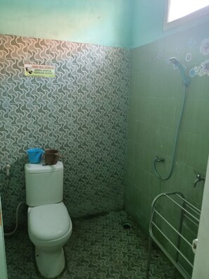 A small bathroom with a toilet, a shower, and a patterned wall. - Griya Sekar Wangi (Surabaya)