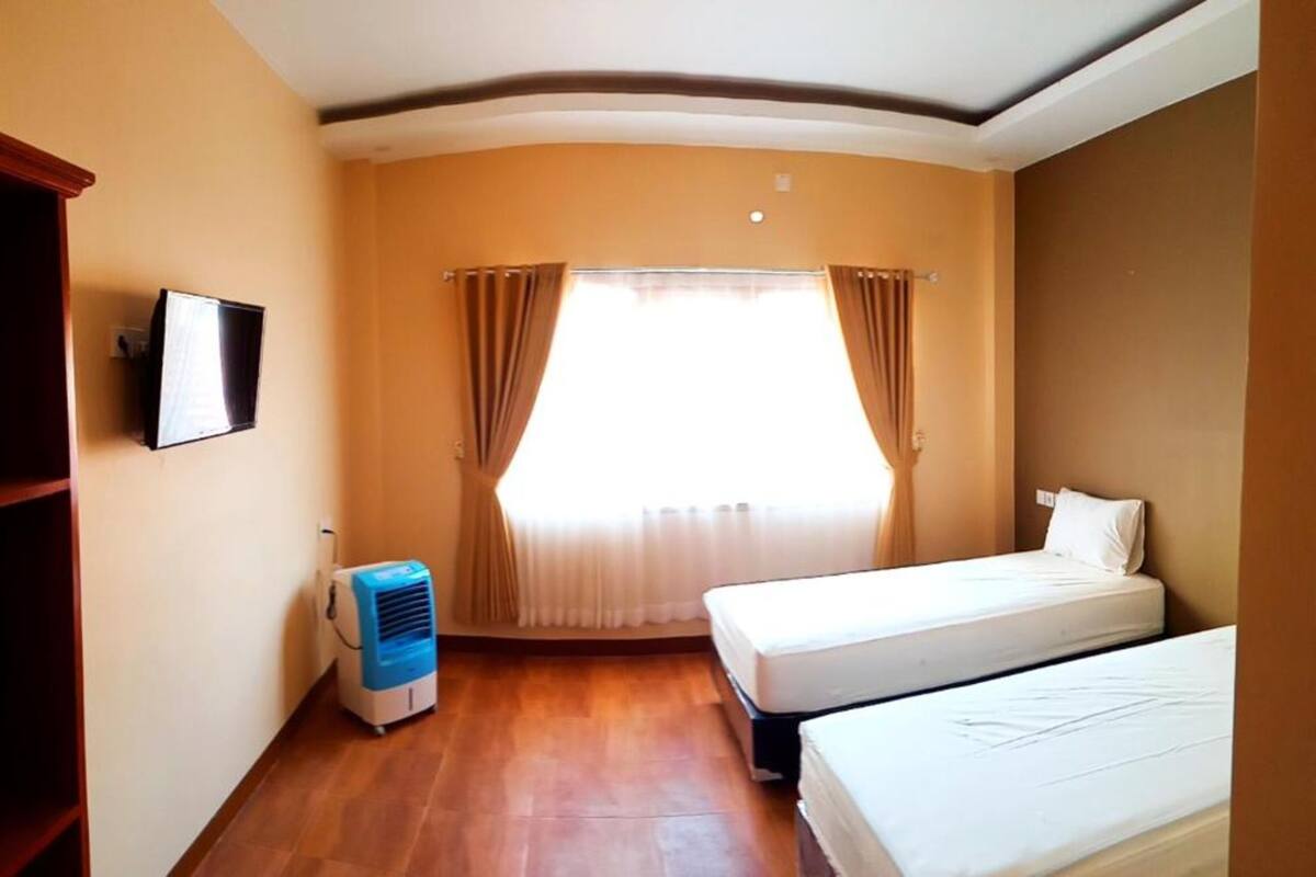 Una camera d'albergo con un letto, una televisione, un termosifone e una finestra con tende.