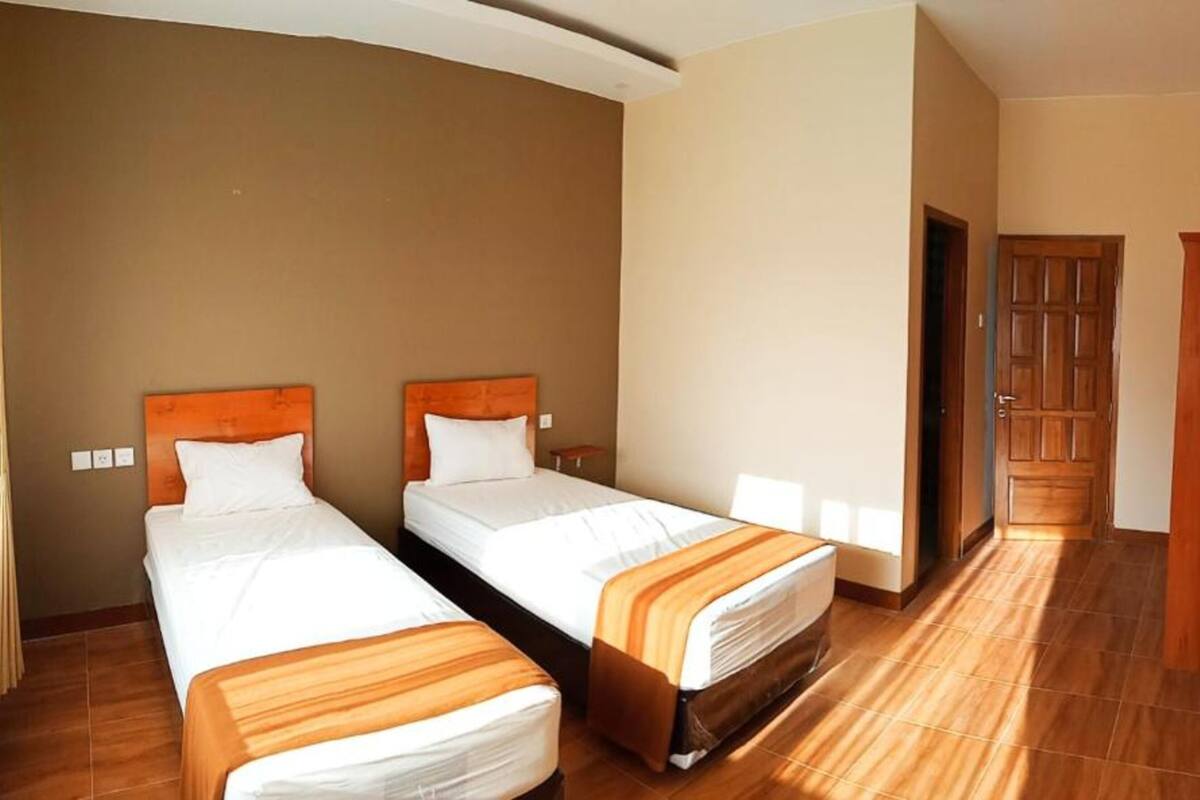 Camera d'albergo con due letti singoli, poggiateste in legno, un armadio in legno e un televisore a parete.