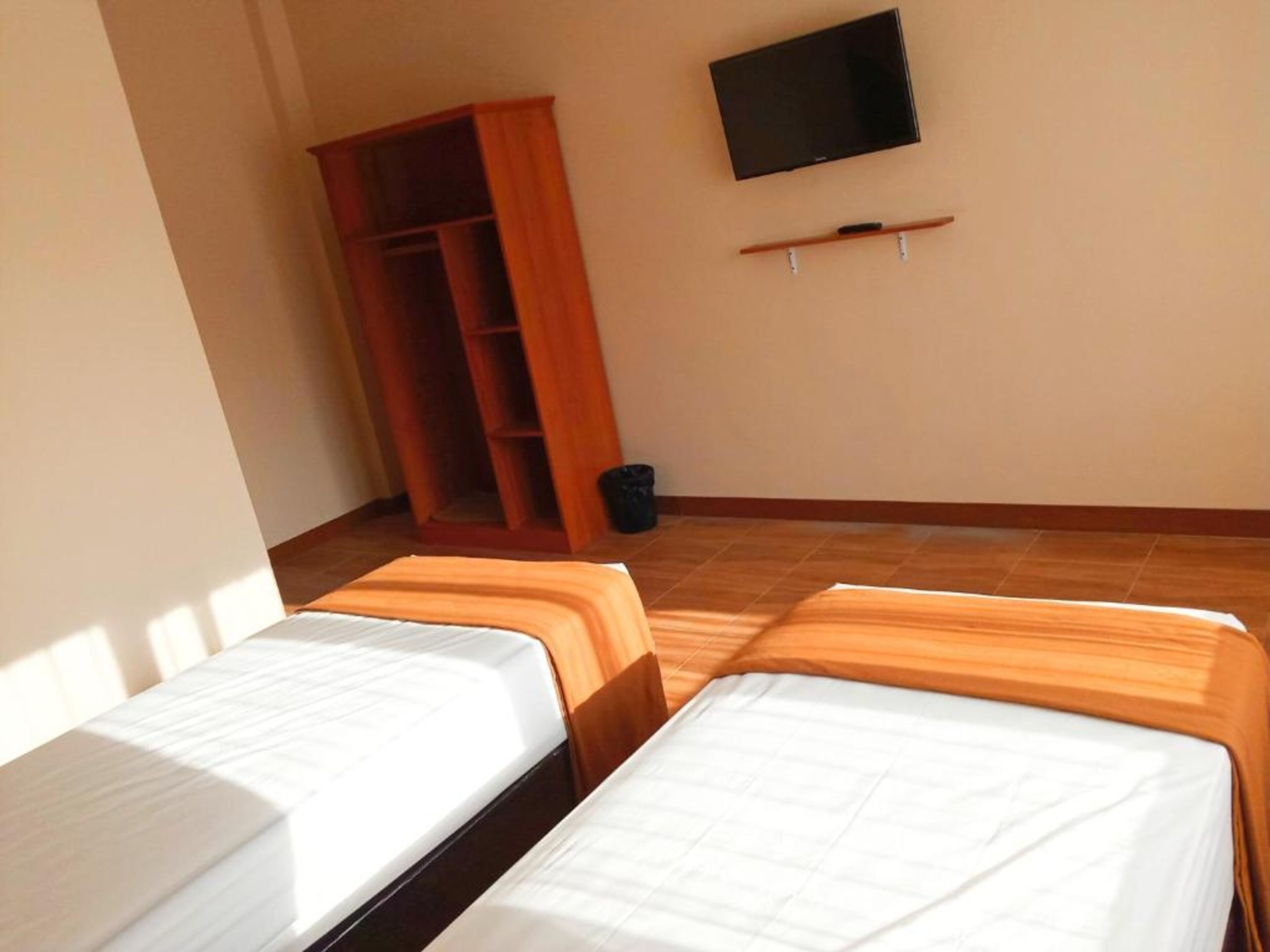 A room with two beds, a TV on the wall, and a wooden wardrobe.