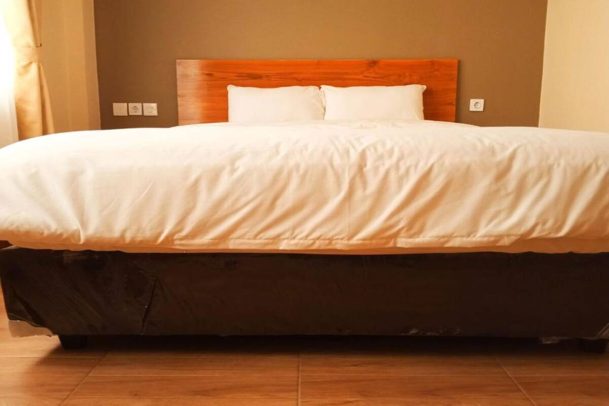 Un letto con testiera in legno, biancheria da letto bianca e un materasso scuro.
