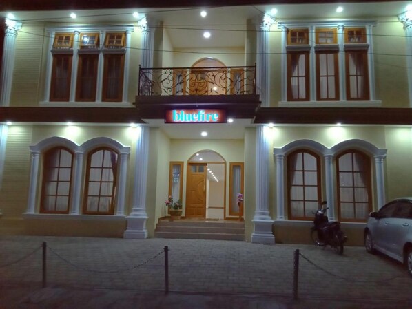 Ein Hotel mit einem zentralen Eingang, einem Balkon mit aufwendiger Geländerarbeit und einem Schild mit der Aufschrift "Bluefire".