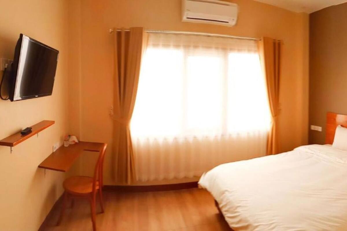 Una camera d'albergo con un letto, una scrivania, una sedia, una televisione e una finestra con tende.